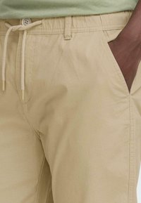 Shorts en coton beige avec une taille élastique, fermeture à cordon et poches latérales. Texture lisse et coupe décontractée.