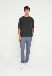 Mørk grå kortermet t-skjorte kombinert med lyseblå slim-fit bukser og hvite sneakers, med et avslappet design og myk tekstur.