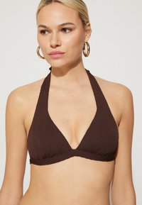 Hnědý pletený bikiny top s designem na krk a trojúhelníkovými košíčky. Texturovaná látka a jednoduchý, minimalistický styl.