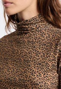 Sweter z golfem w print w panterę w odcieniach brązu i czerni, wykonany z miękkiej tkaniny o dopasowanym kroju i wysokim kołnierzu.