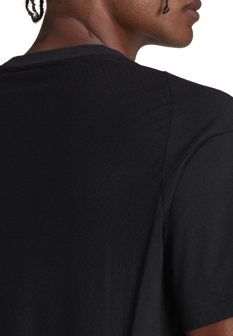 Camisa negra de manga corta con un patrón texturizado, que presenta un cuello redondo y una tela suave. La parte posterior muestra un acabado limpio y detalles sutiles.