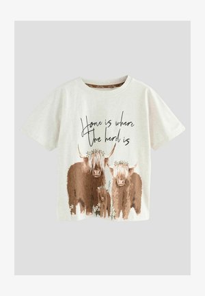 T-shirt beige clair avec une illustration de trois vaches de haute lande ornées de fleurs et du texte "Chez soi, c'est là où est le troupeau" en dessous.