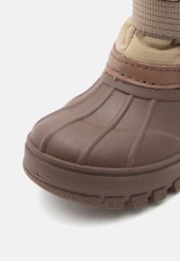 Bota marrón impermeable con sección inferior de goma, acabado texturizado y parte superior reforzada. Presenta un diseño suave y ligeramente acolchado.