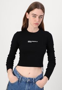 Schwarzes, geripptes Cropped-Top mit langen Ärmeln und Rundhalsausschnitt, auf der Brust mit weißer Stickerei "KARL LAGERFELD JEANS".