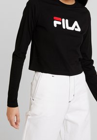 Svart långärmad cropped tröja med röd och vit "FILA" logotyp. Matchad med höga vita byxor med kontrasterande sömmar.
