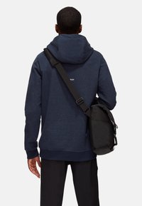 Granatowy hoodie z regulowanym kapturem i ściągaczami na rękawach, noszony z czarną torbą na ramię. Gładki materiał o luźnym kroju i minimalnym oznakowaniu.