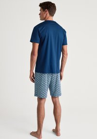 Marineblauw T-shirt met korte mouwen en een ronde hals, gecombineerd met gebloemde blauwe shorts met een geometrisch design. Zachte stof, casual fit.