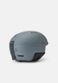Casco de esquí gris con un acabado mate, que cuenta con orificios de ventilación, una correa para la barbilla y un acento negro texturizado en la base.