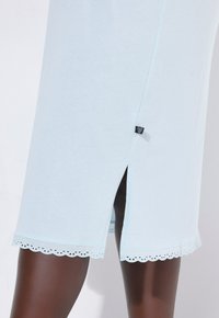 Světle modré bavlněné šaty s krajkovým lemem s obloukovým vzorem a bočními rozparky, se malou značkovou štítkem u švu. Hladká textura.