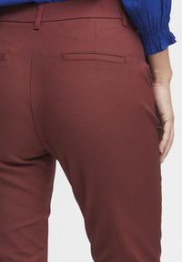 Burgundiska byxor med en slät yta, som har en figursydd design och sidfickor. Midjan är platt med en subtil sömdetalj.