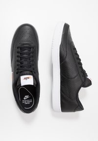 Svarta lädersneakers med texturerad yta, vit gummisula och svarta snören. Har logotypmärke på tungan och diskret varumärkning på sidan.