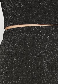 Svart ribbad stickad tvådelad set som består av en kort topp och högmidjade underdelar, prydda med glittrande silverprickar.