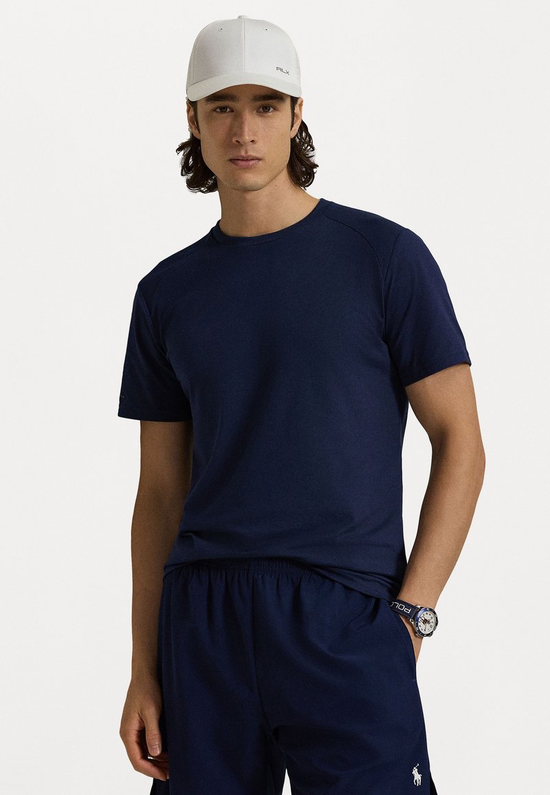 Σκούρο μπλε κοντομάνικο μπλουζάκι, λαιμόκοψη σε στιλ crew, με ομαλή υφή. Συνδυάζεται με ταιριαστά σορτς, που διαθέτουν ελαστική μέση και λεπτομέρεια λογότυπου.