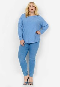 Šviesiai mėlyna ilgomis rankovėmis palaidinė su laisvu siluetu, derinama su šviesiai mėlynais siaurais džinsais. Audinys atrodo minkštas, be ryškių raštų.