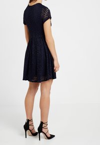 Námořnické krajkové šaty s krátkými rukávy a rozšířenou sukní; mají květinový vzor. Nosené s černými lodičkami na vysokém podpatku s křížovými popruhy.