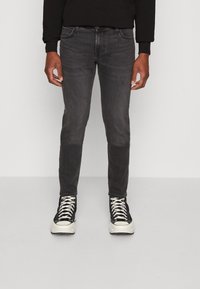 Jean en denim gris foncé, coupe slim, avec une texture légèrement usée. Associé à des baskets montantes noires avec des accents et des lacets blancs.