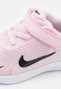 Baskets de sport roses avec un dessus en mesh, semelle en caoutchouc et logo Swoosh noir de Nike. Comprend des lacets élastiques et une sangle en Velcro pour un ajustement sécurisé.