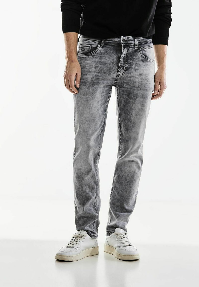 Helle graue Jeans aus Denim mit einem ausgewaschenen Textur, schmaler Schnitt, fünf Taschen und Gürtelschlaufen, kombiniert mit weißen Sneakers.