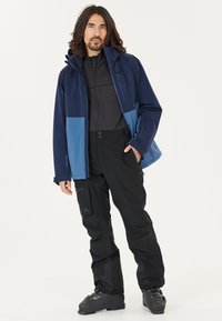 Heren buitenjack in marineblauw en lichtblauw, gecombineerd met zwarte waterdichte broek. Bevat ritsen, zakken en een gestructureerde stof voor duurzaamheid.