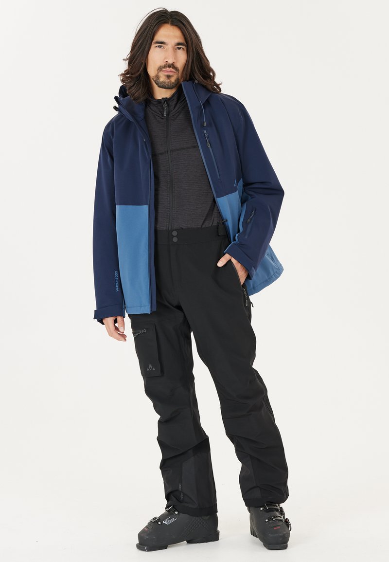 Heren buitenjack in marineblauw en lichtblauw, gecombineerd met zwarte waterdichte broek. Bevat ritsen, zakken en een gestructureerde stof voor duurzaamheid.