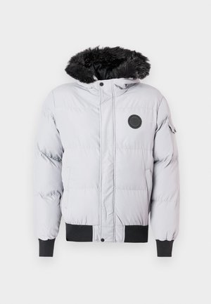 Hallide hallenilt mütsiga hall puffer-jacket, ribakäiste ja -äärtega. Omab ümmargust logopatchi rinnal ja esiakarpi.