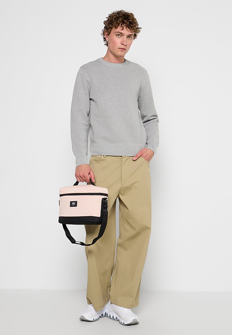 Suéter gris, pantalones caqui, zapatillas blancas. Sosteniendo un pequeño bolso rosa y negro con una correa para el hombro y herrajes negros.