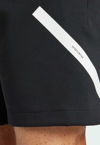 Shorts sportivi neri realizzati in tessuto testurizzato, con una striscia bianca diagonale e un logo con la scritta "SPORTSWEAR" di lato.