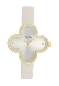 Montre ronde avec un cadran argenté brillant, des accents dorés et un bracelet beige. Présente une forme de trèfle et des marqueurs d'heure minimalistes.