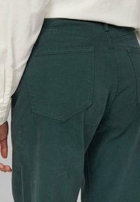 Grüne Baumwollhose mit strukturierter Oberfläche, ausgestattet mit zwei Gesäßtaschen und dezenten Steppnähten.