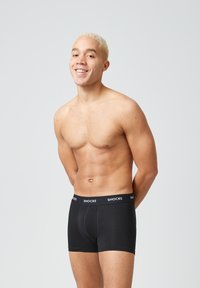 Zwarte boxershorts met een strakke pasvorm en elastische tailleband, waarin de merknaam "SNOCKS" in het wit is gedrukt. Soepele textuur tegen blote huid.