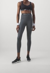 černá sportovní podprsenka s širokými pásky a značkou Nike; šedé legíny s vysokým pasem a logem na boku; černé sportovní boty.