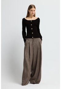 Svart ribbstickad tröja med vid halsringning och guldfärgade knappar, kombinerad med bruna plisserade vida byxor i ett texturerat tyg.