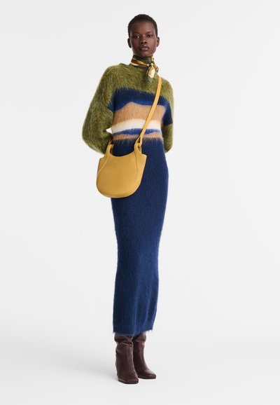 Gestreifter Strickpullover in grün, blau und beige; eng anliegender, langer, fusseliger blauer Rock; braune knielange Stiefel; gelbe Leder-Schultertasche.