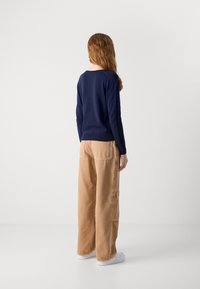 Maglione a maglia blu navy con scollo rotondo, abbinato a pantaloni cargo beige a gamba larga con tasche laterali; sneakers bianche completano l'outfit.