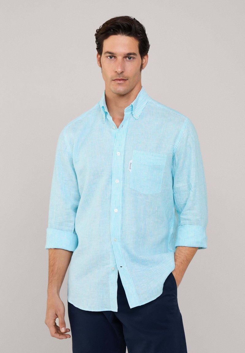 Camisa de botones a rayas azul claro con mangas largas arremangadas hasta los codos, que cuenta con un bolsillo en el pecho y una textura de tela suave.