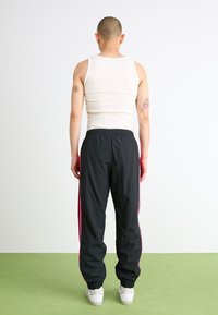 Pantaloni sportivi neri con strisce rosa ai lati, vita elasticizzata e caviglie impunturate. Maglietta bianca senza maniche. Persona vista da dietro.