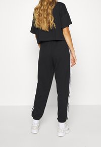 Svart kort topp och tapered joggers med vita sidostrimmor. Mjuk tyg, avslappnad passform, kombinerad med vita sneakers.