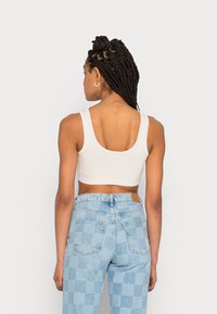 Top cropped branco com alças largas e costas baixas, combinado com jeans de cintura alta em padrão xadrez azul claro. Textura de algodão suave.