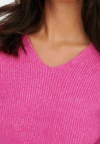 V-Ausschnitt Pullover in leuchtendem Pink. Gerippte Textur mit glatter Oberfläche. Weiches Material, taillierter Schnitt ist um Hals und Schultern sichtbar.