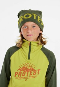 Groene beanie met "PROTEST" in het geel, en een groen en lichtgroen zip-up shirt met een bergafbeelding en oranje tekst.