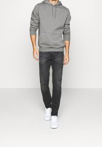 Sudadera de algodón gris con cordón, combinada con jeans de mezclilla oscura y zapatillas blancas. Diseño simple sin patrones ni logotipos visibles.