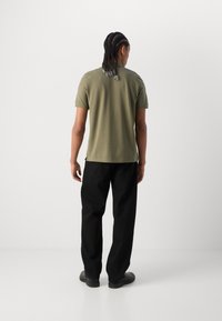 Tricou scurt cu maneci verzi măslinii, cu croială dreaptă, asociat cu pantaloni negri cu croială dreaptă și pantofi negri. Material neted, detalii minime.