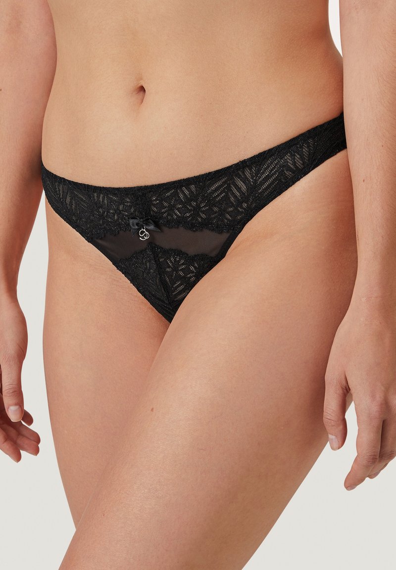 String noir en dentelle avec des motifs floraux, des panneaux en tulle transparent et un petit nœud en satin à l'avant. Côtés réglables pour un ajustement parfait.