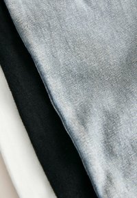 Three t-shirts arranged in layers: a light blue, a black, and a white. All are made of soft, smooth fabric with a fine texture.