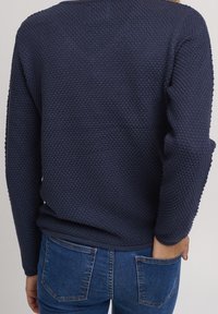 Navyblauer strukturierter Pullover mit lockerer Passform, langen Ärmeln und gerundetem Ausschnitt, kombiniert mit blauen Jeans.