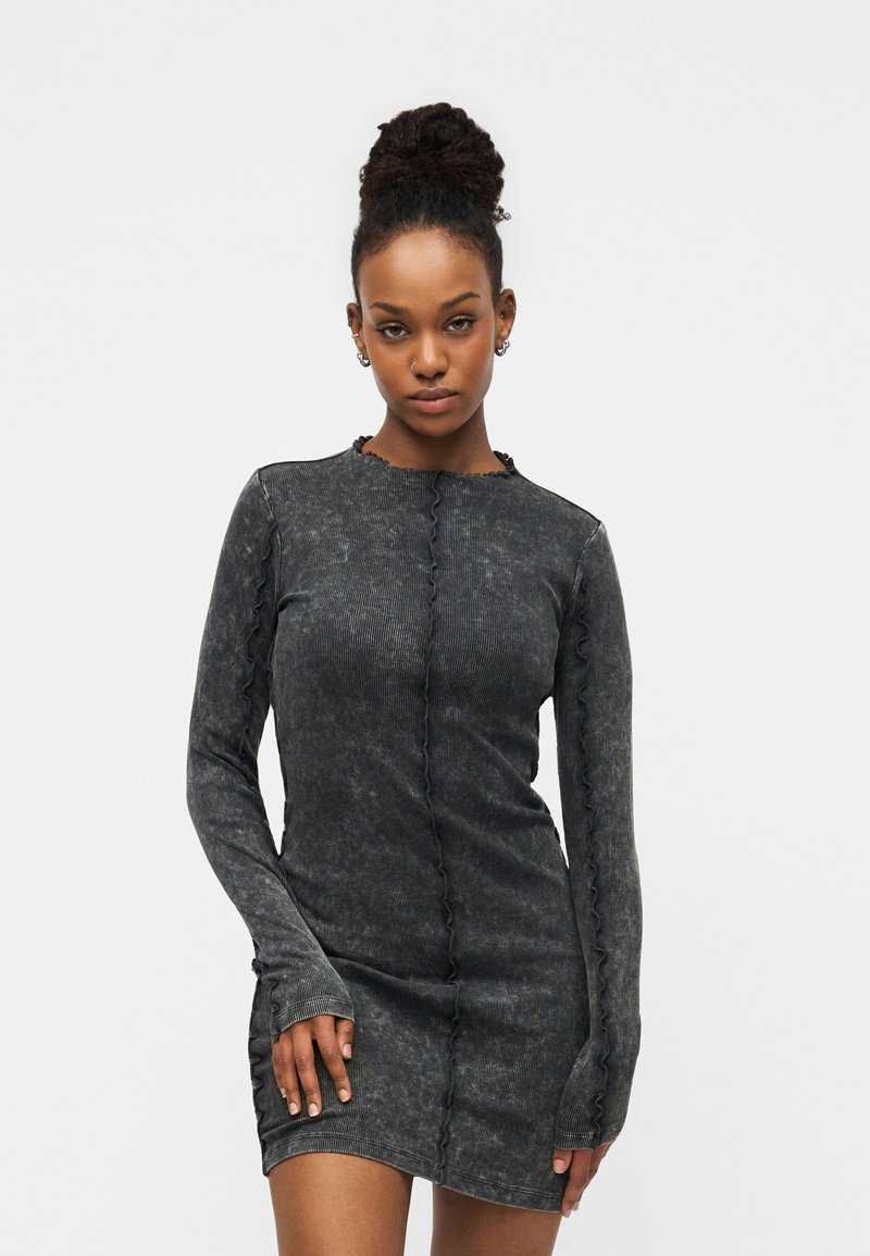 Φόρεμα με μακριά μανίκια σε σκουρό γκρι χρώμα, με ριμπ ύφανση και βολάν κατά μήκος των ακρών. Στενή εφαρμογή με στρογγυλή λαιμόκοψη.