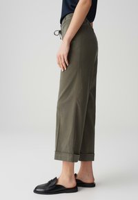 Olive green wide-leg trousers with a drawstring waist, cuffed hem, and smooth fabric finish, paired with black slip-on shoes.