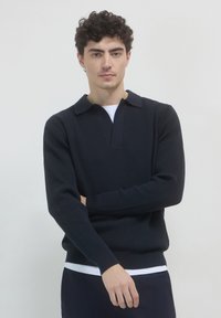 Pull en tricot côtelé bleu marine foncé avec des manches longues, un col et un décolleté en V. Couleur unie et finition texturée.