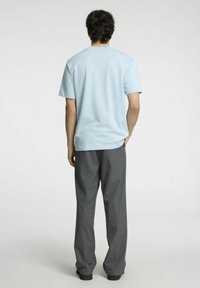 Šviesiai mėlynas medvilninis marškinėlis su trumpomis rankovėmis, derinamas su laisvai krentantimis tamsiai pilkomis kelnėmis. Paprastas, nepuošiamas galinis vaizdas be raštų ar grafikos.