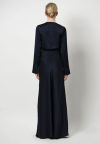 Långärmad, golvlång klänning i marinblå texturerad tyg, med en figursydd midja och detalj vid ryggen. Inga synliga mönster eller accenter.